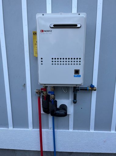 Wall-mounted white utility box with pipes, valves, and a gas meter on a striped exterior wall.