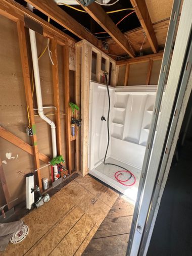 Unfinished bathroom with exposed studs, a white shower base, and plumbing visible near the floor.