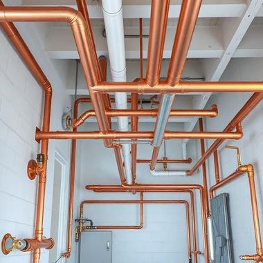Copper pipes and white ductwork on a utility room ceiling above gray cabinets and cinder block walls