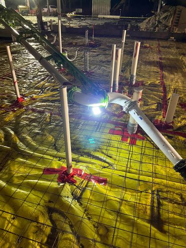 Nighttime construction site with bright work light, wooden stakes, and wet ground under scaffolding remnants