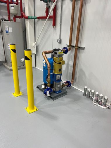 Industrial equipment with yellow safety bollards, copper pipes, and a blue pump in a utility room