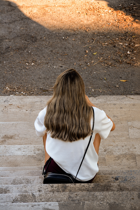 Frau sitzt nachdenklich auf einer Treppe – Symbolbild für die Krise nach einer Affäre
