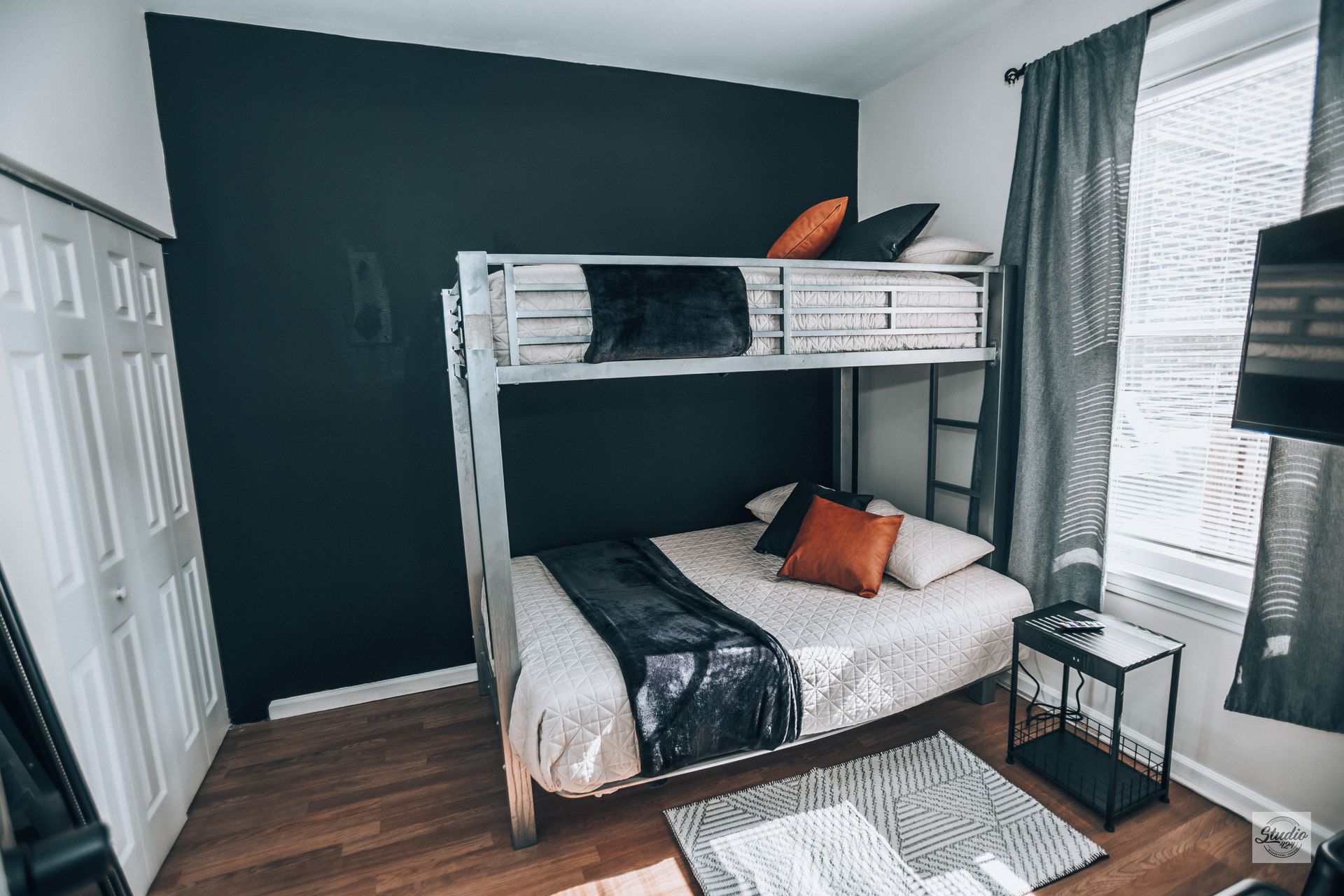 Bunk beds in a room with black accent wall, window, and small rug.