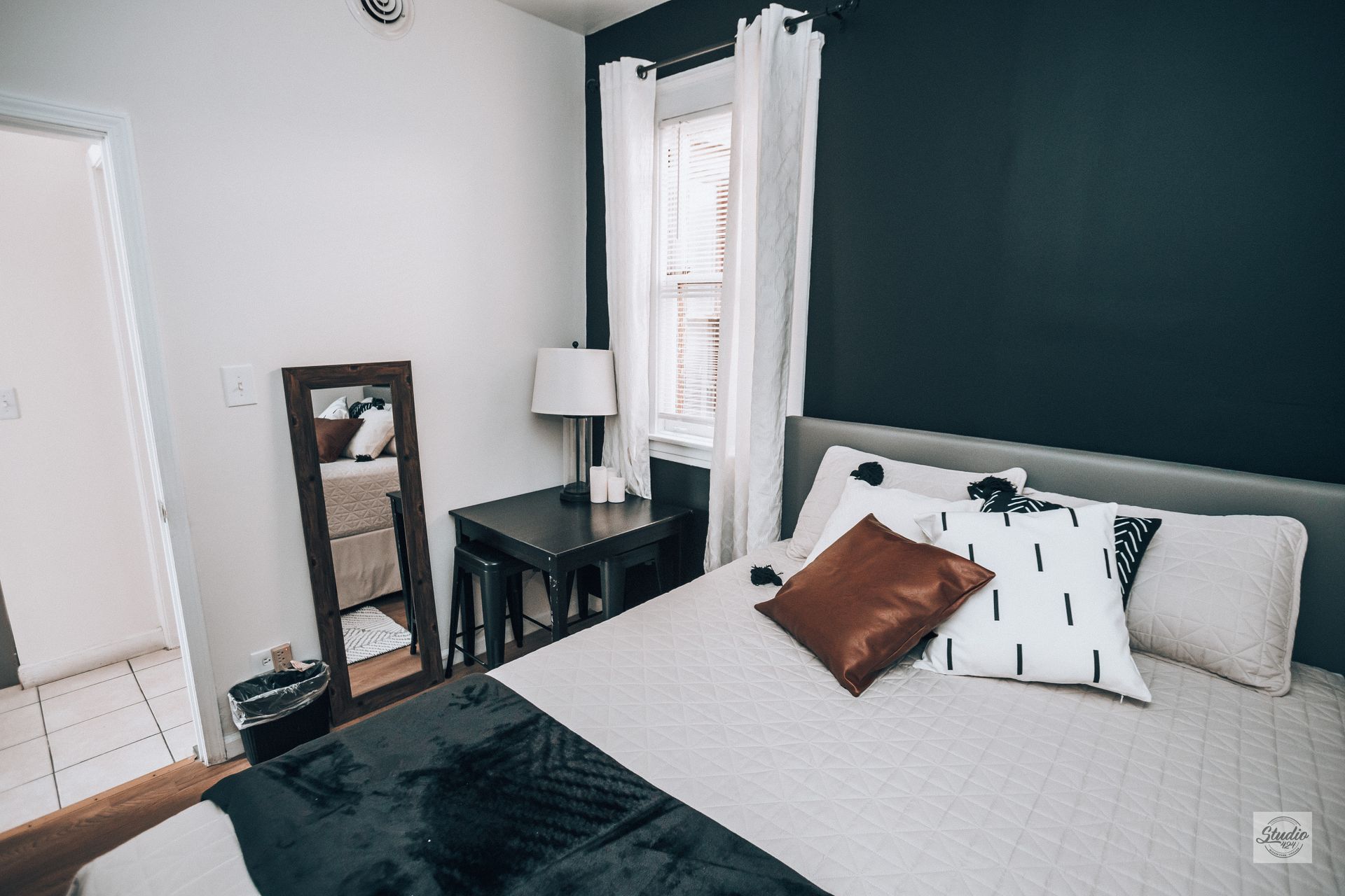 Bedroom with bed, dark accent wall, mirror, nightstand, and window.