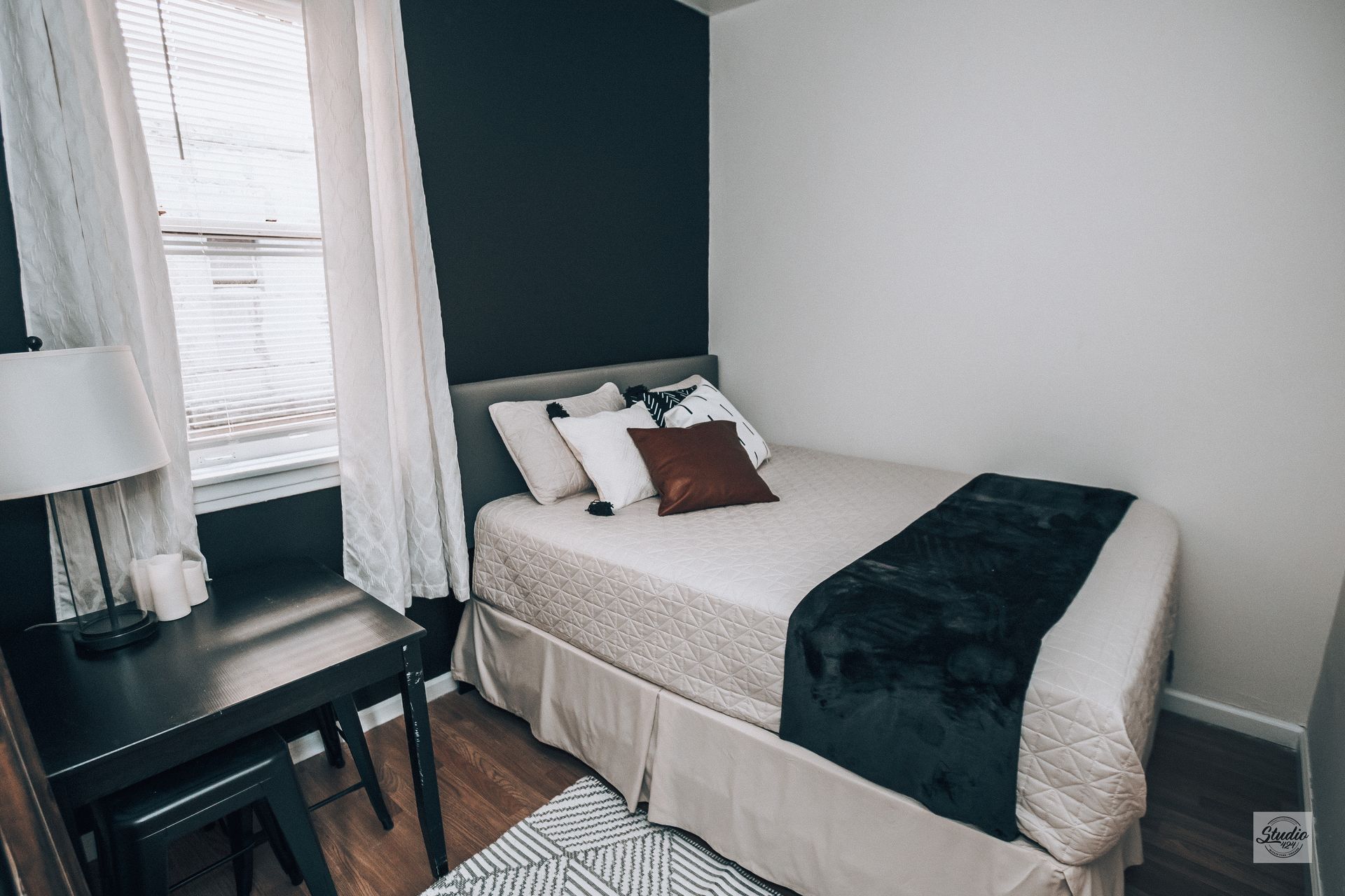 Small bedroom with a bed, desk, and window. One wall is dark blue, the others white.