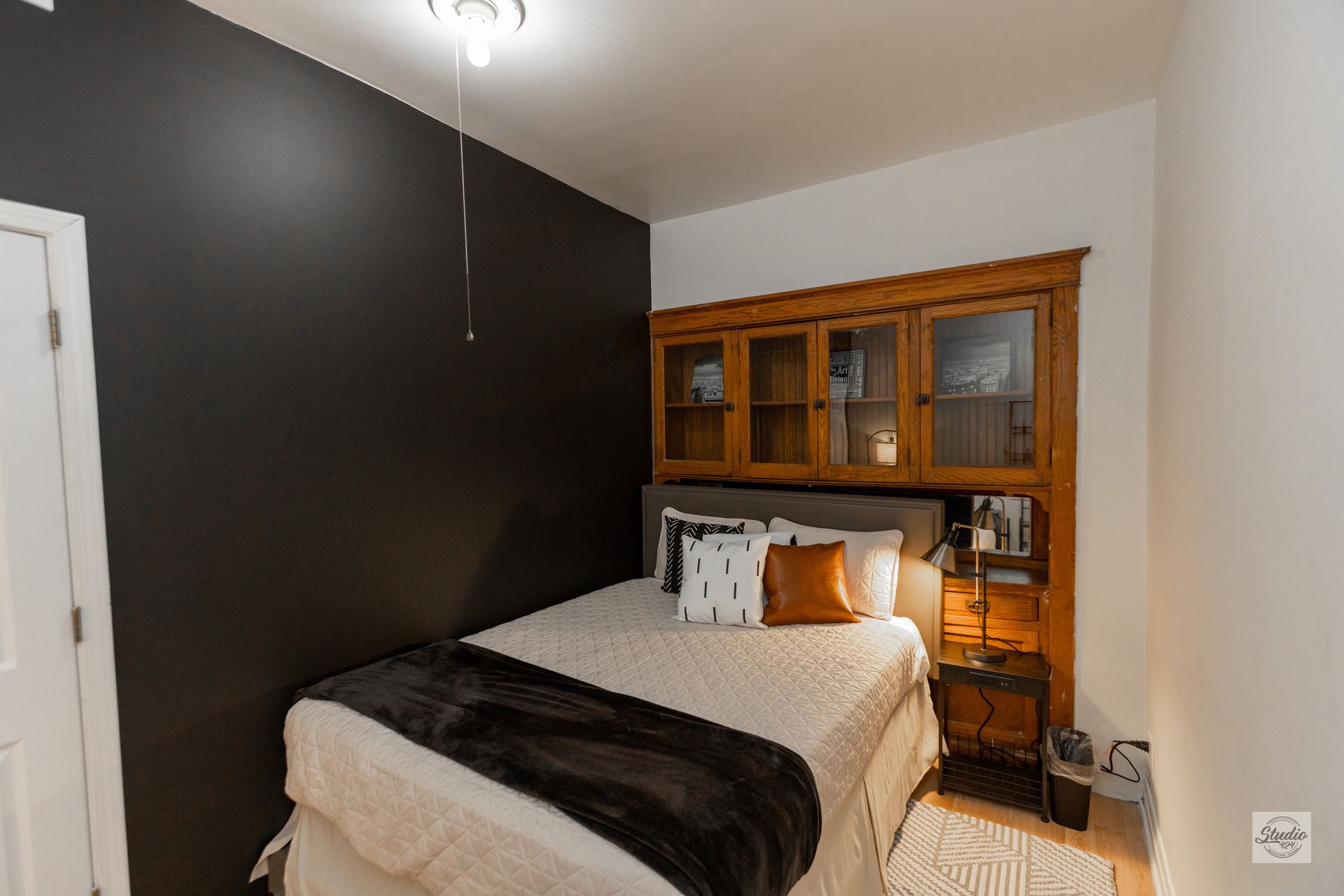 Bedroom with bed, dark accent wall, wooden storage cabinets, and a nightstand.