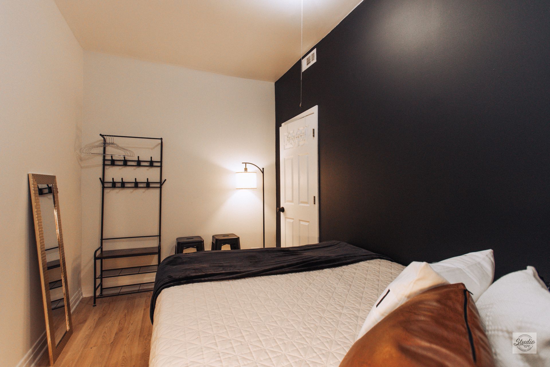 Bedroom with a bed, dark accent wall, a shelving unit, and a floor lamp.