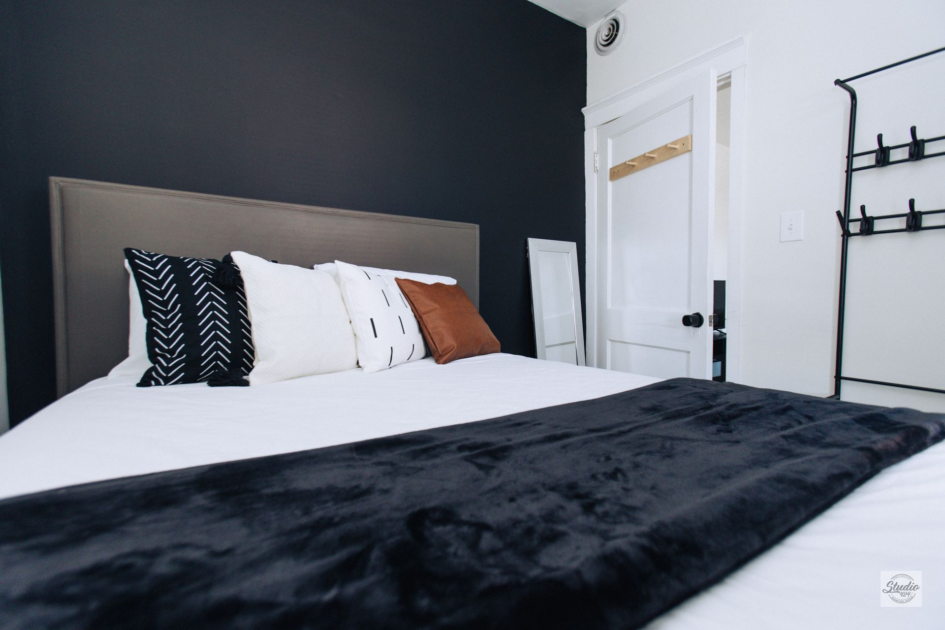 Bedroom with a dark blue wall, a bed with pillows and a black blanket, and a decorative rack.