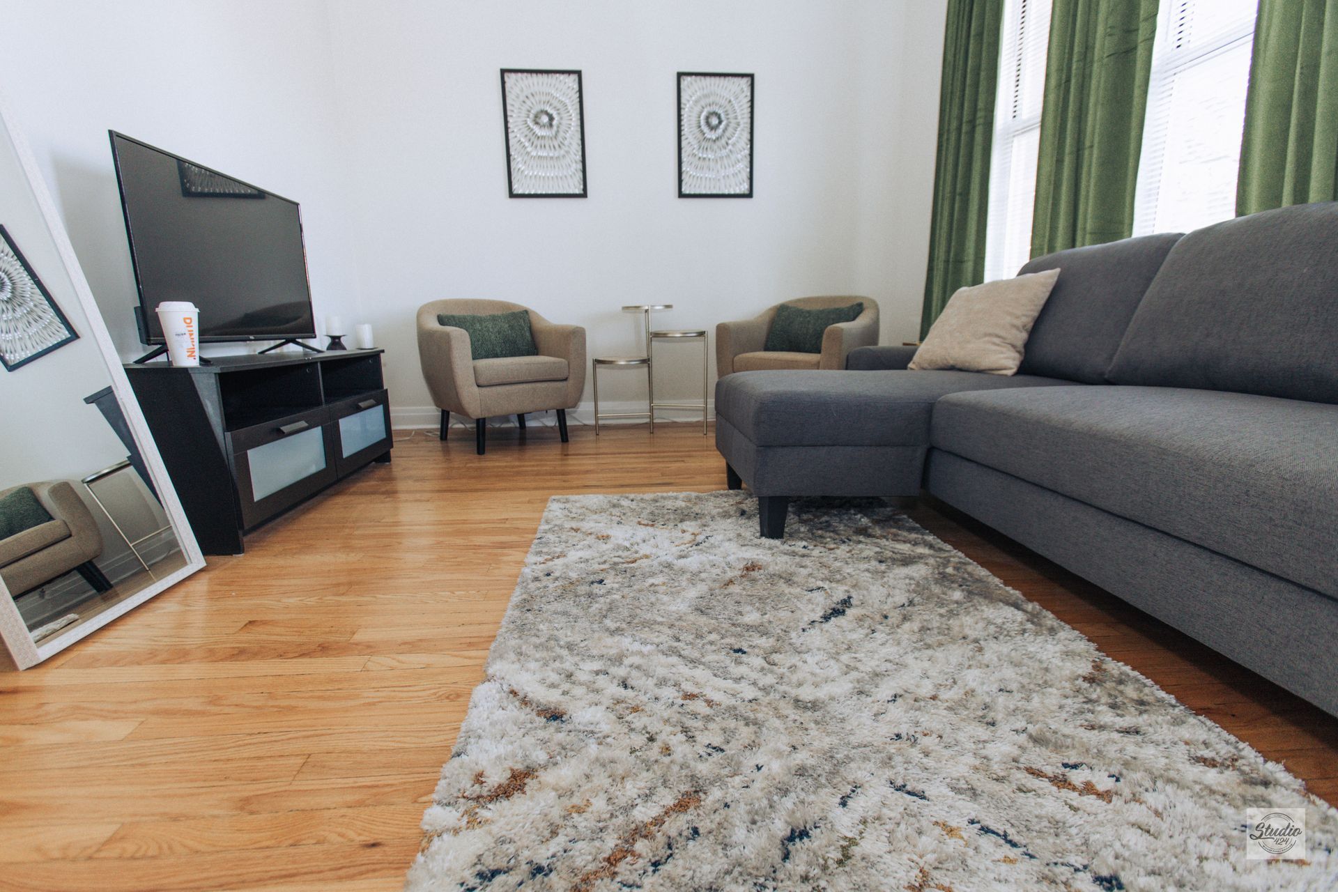 Living room with gray sectional sofa, rug, TV, armchairs, mirror, and two framed prints.