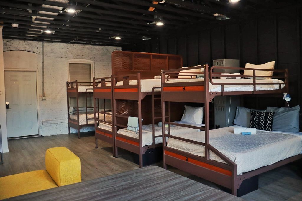 Bunk beds in a room with a yellow ottoman and open door. Walls are black, white, and wood-toned.