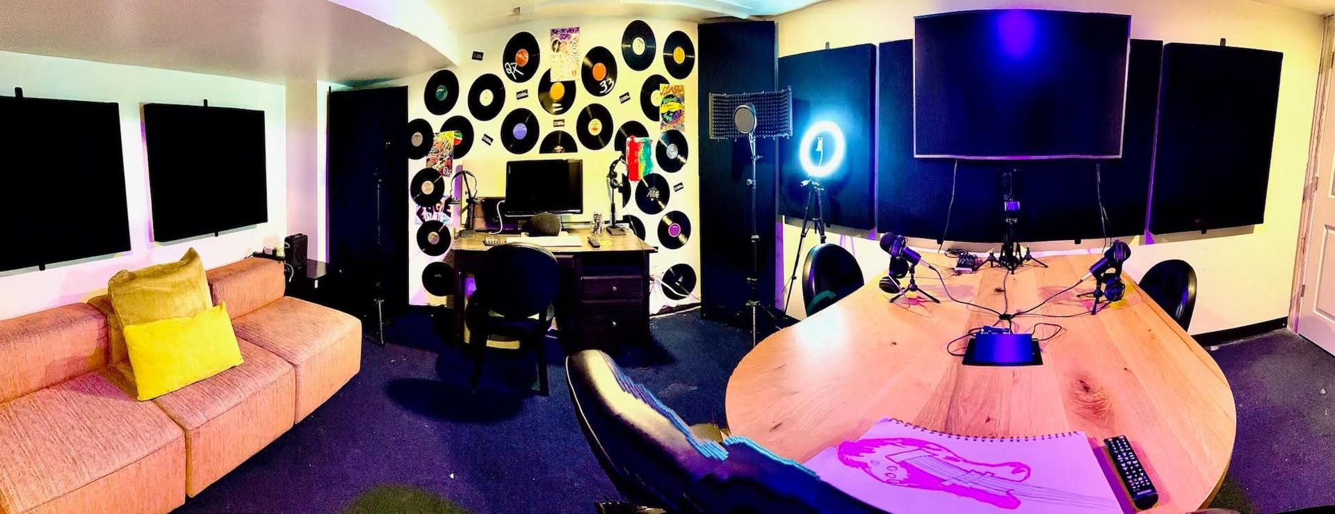 Recording studio with a couch, desk, and soundproofing. Vinyl records on the wall.
