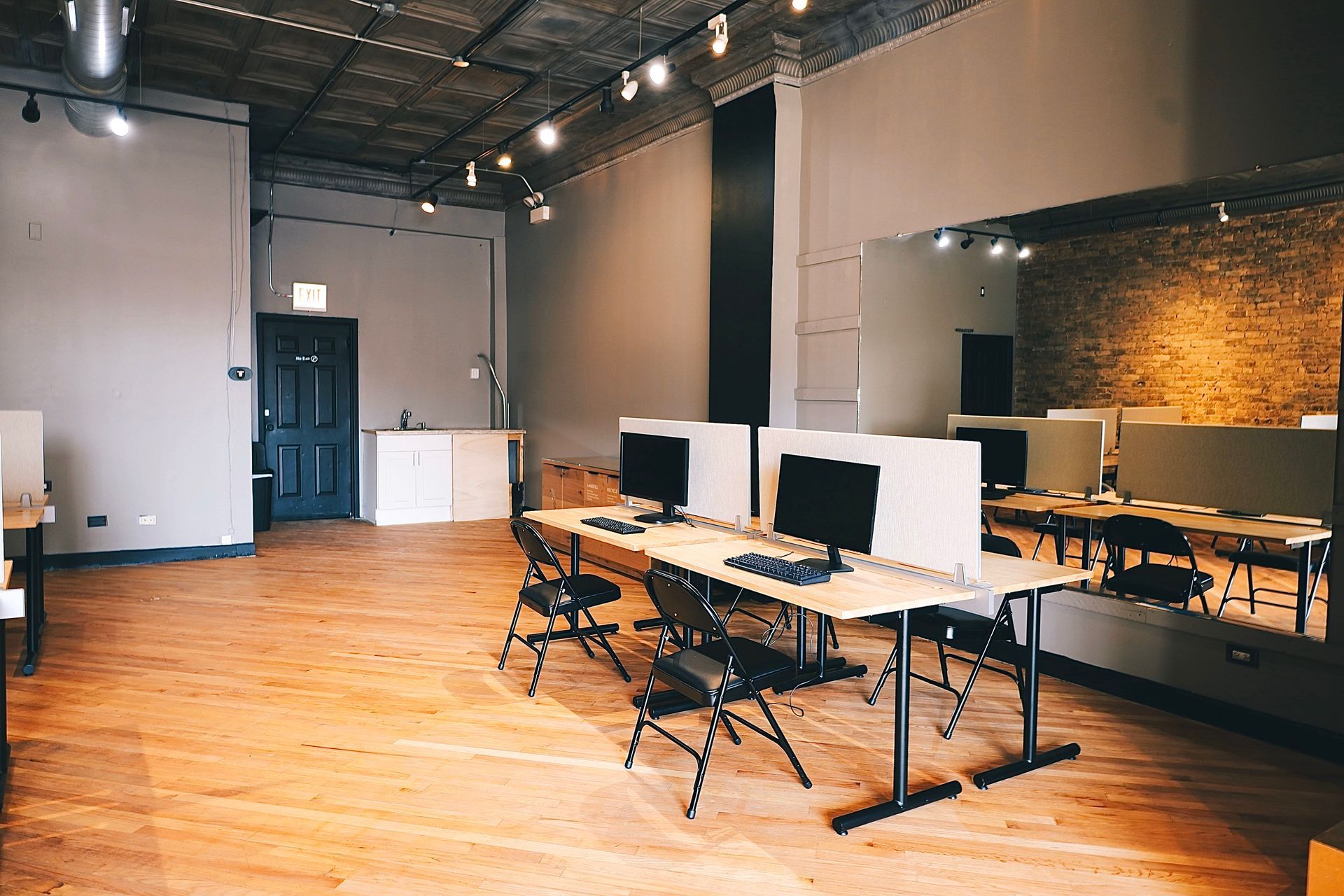 Empty office with computer desks, chairs, wood floor, and exposed ceiling.