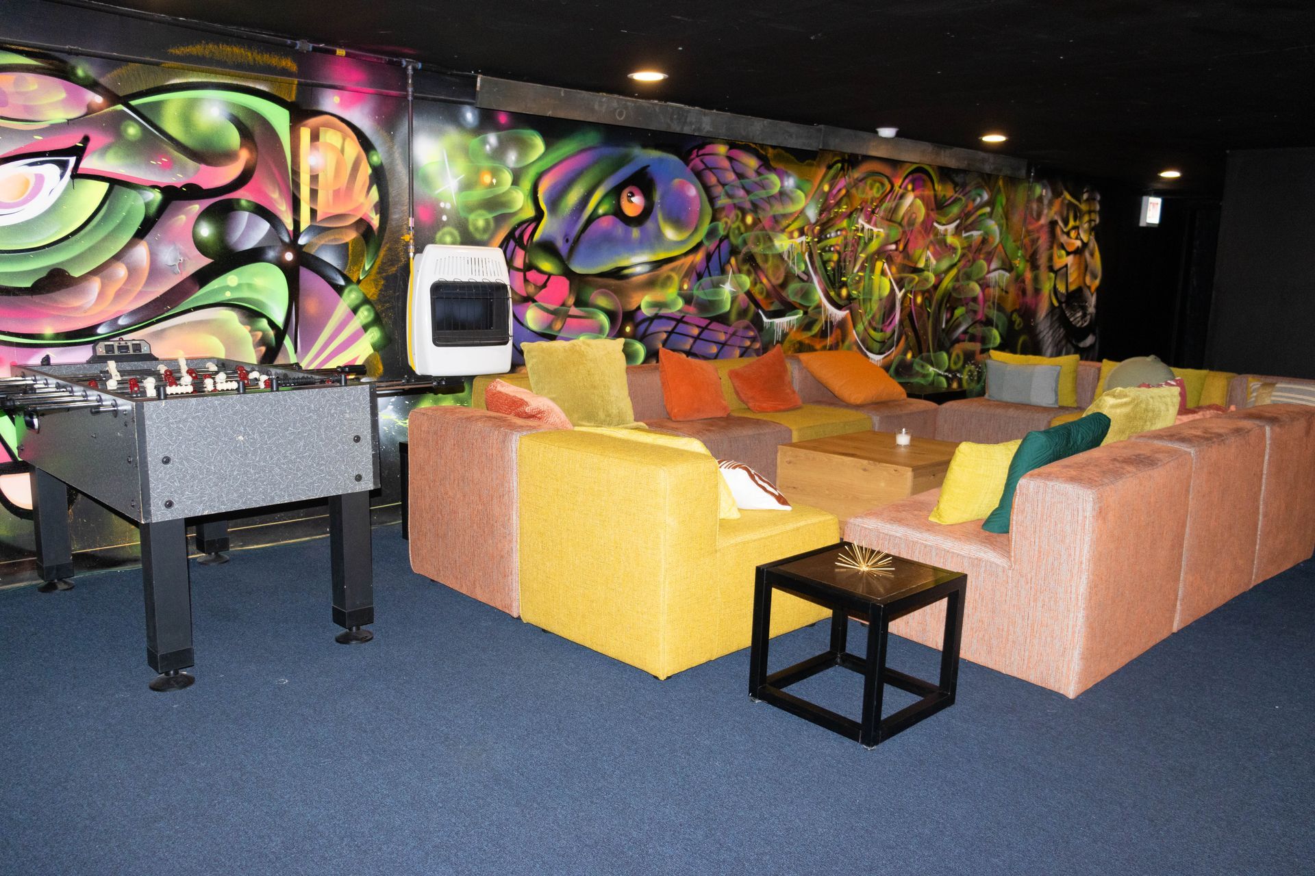 Game room with foosball table, large colorful graffiti wall, and modular sofas with various colored cushions.