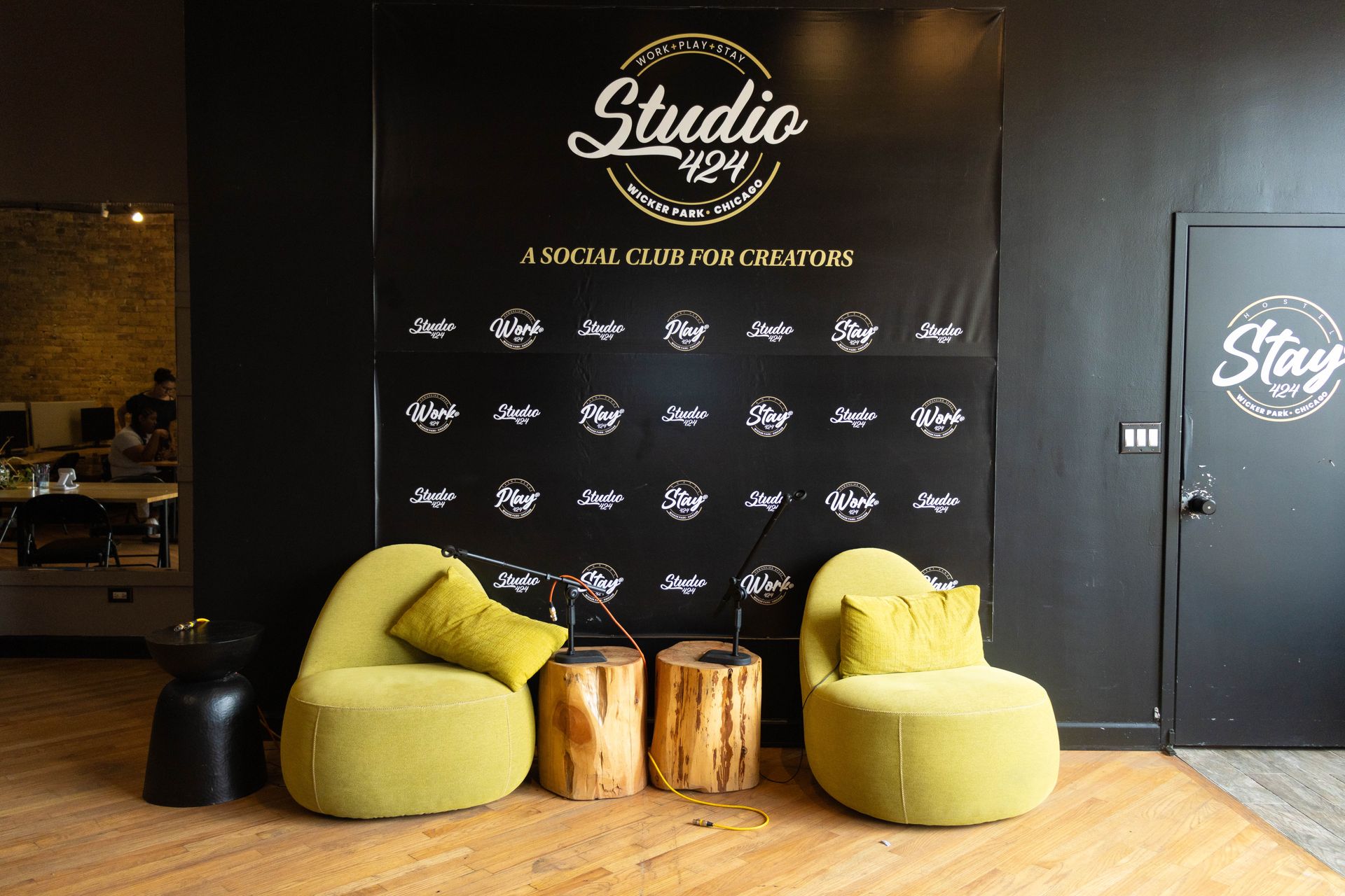 A lounge area in Studio 429. Two green chairs face a wall with logos; tree trunk side tables.
