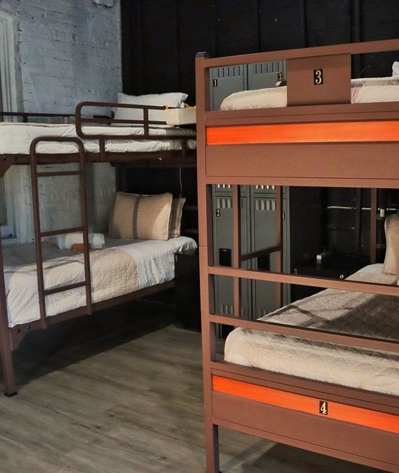 Bunk beds in a room. Brown metal frames with orange accents. Lockers are in the background.