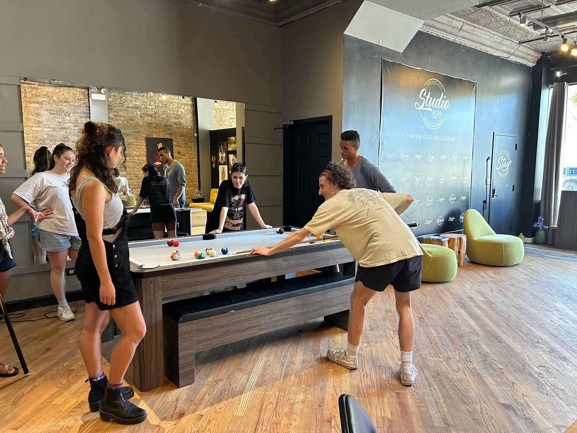 People playing pool in a room with hardwood floors, a large mirror, and modern decor.