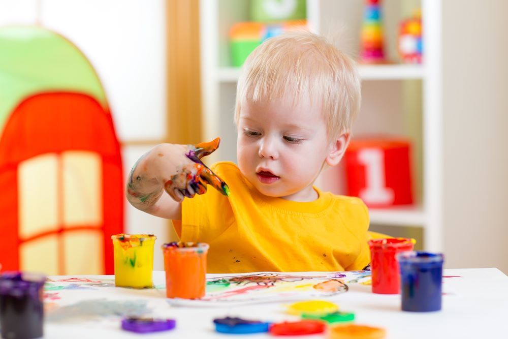 A Little Boy is Sitting at a Table Playing With Paint — Grandma Rosie’s Quality Long Day Care In Horsley, NSW