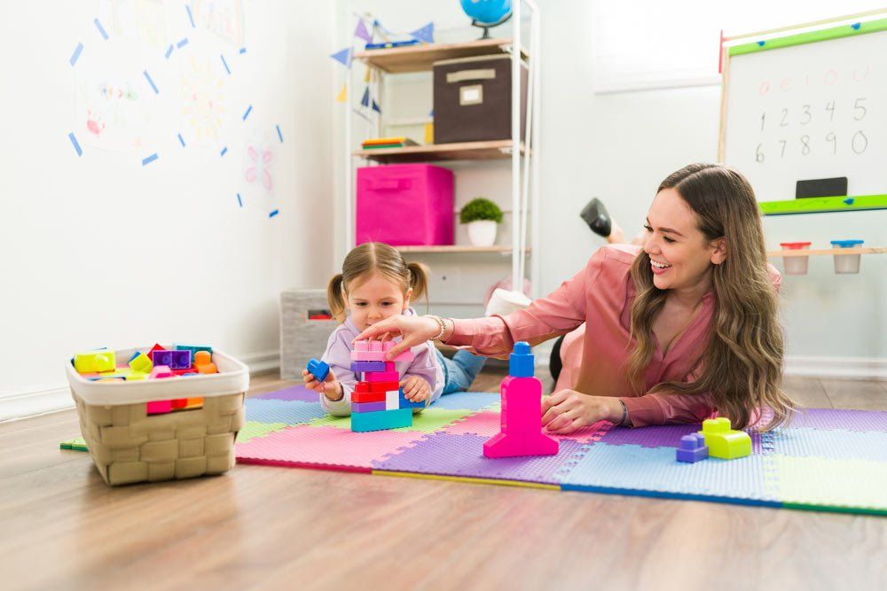 Smiling Teacher With Little Girl Playing Blocks — Grandma Rosie’s Quality Long Day Care In Wollongong, NSW