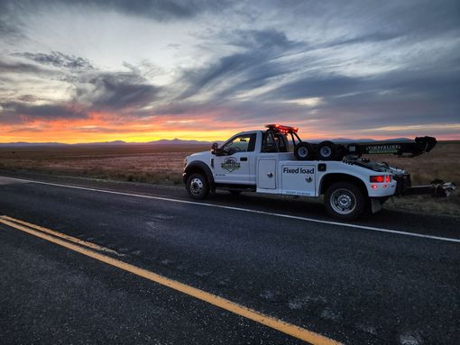 A white tow truck is parked on the side of the road at sunset.