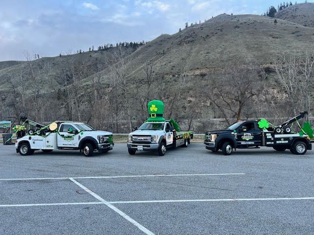 Three utility trucks with green emergency signs parked in a lot beside a rocky hillside