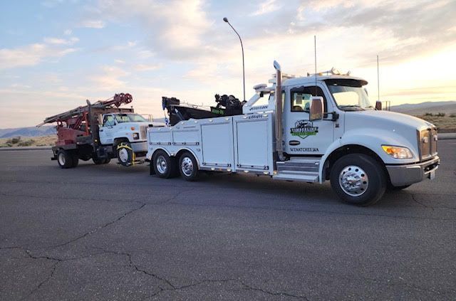 White tow truck hauling a red car on a flatbed at dusk in a parking lot