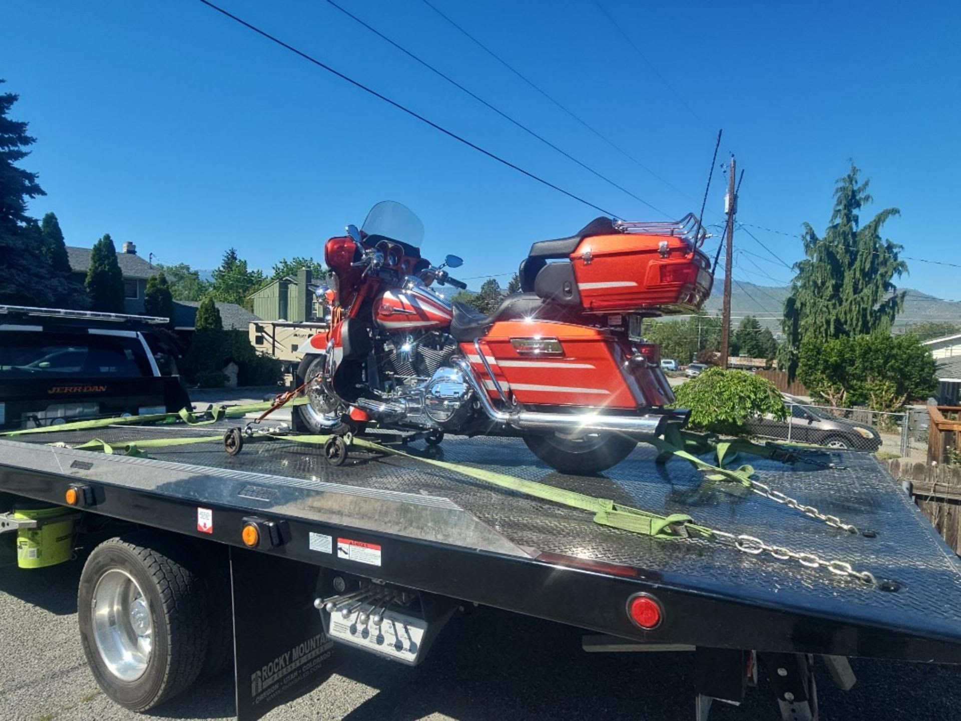 Red touring motorcycle strapped on a black trailer outdoors under a clear blue sky.
