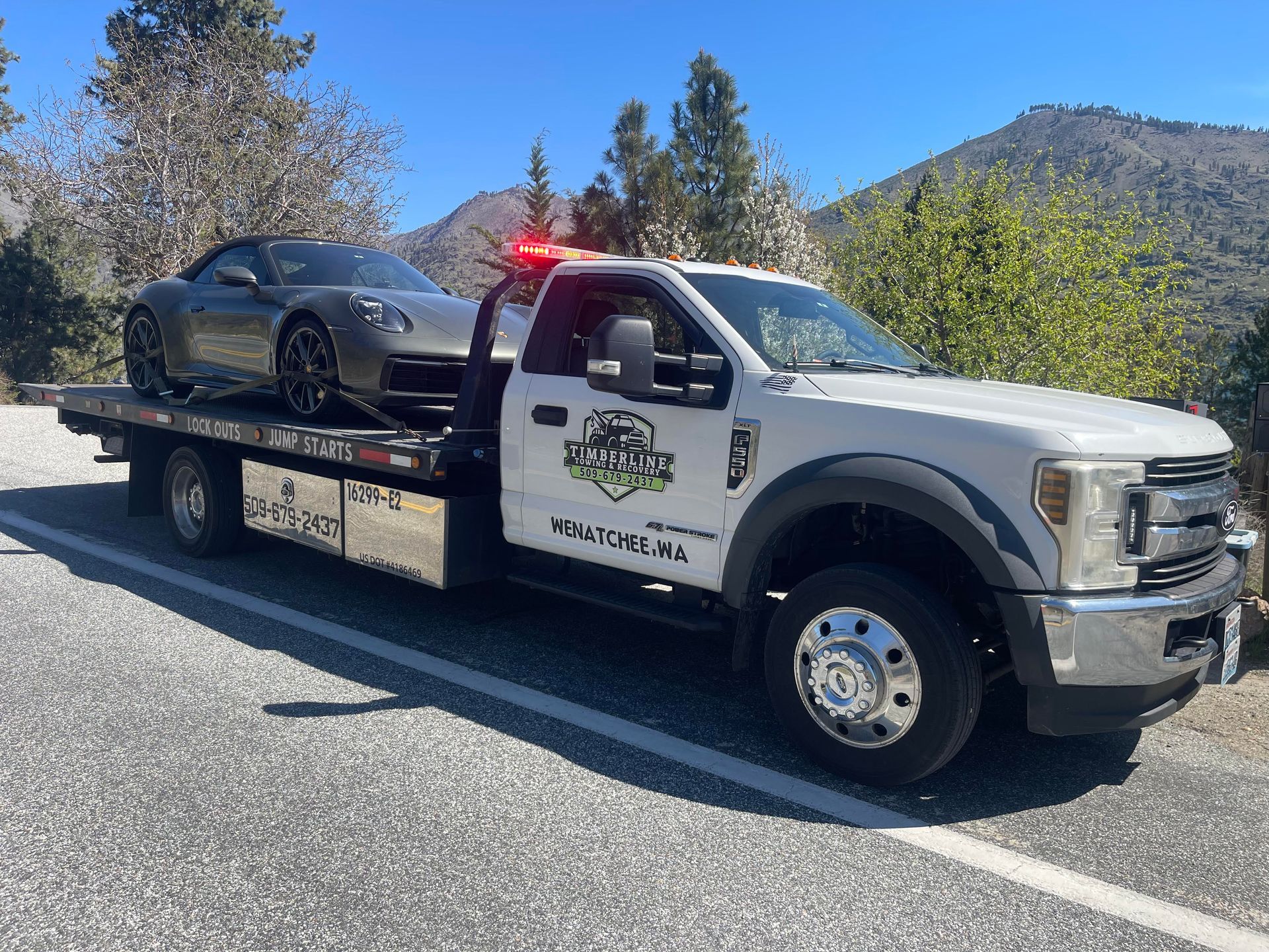 Tow truck hauling a black car on a roadside with mountains in the background