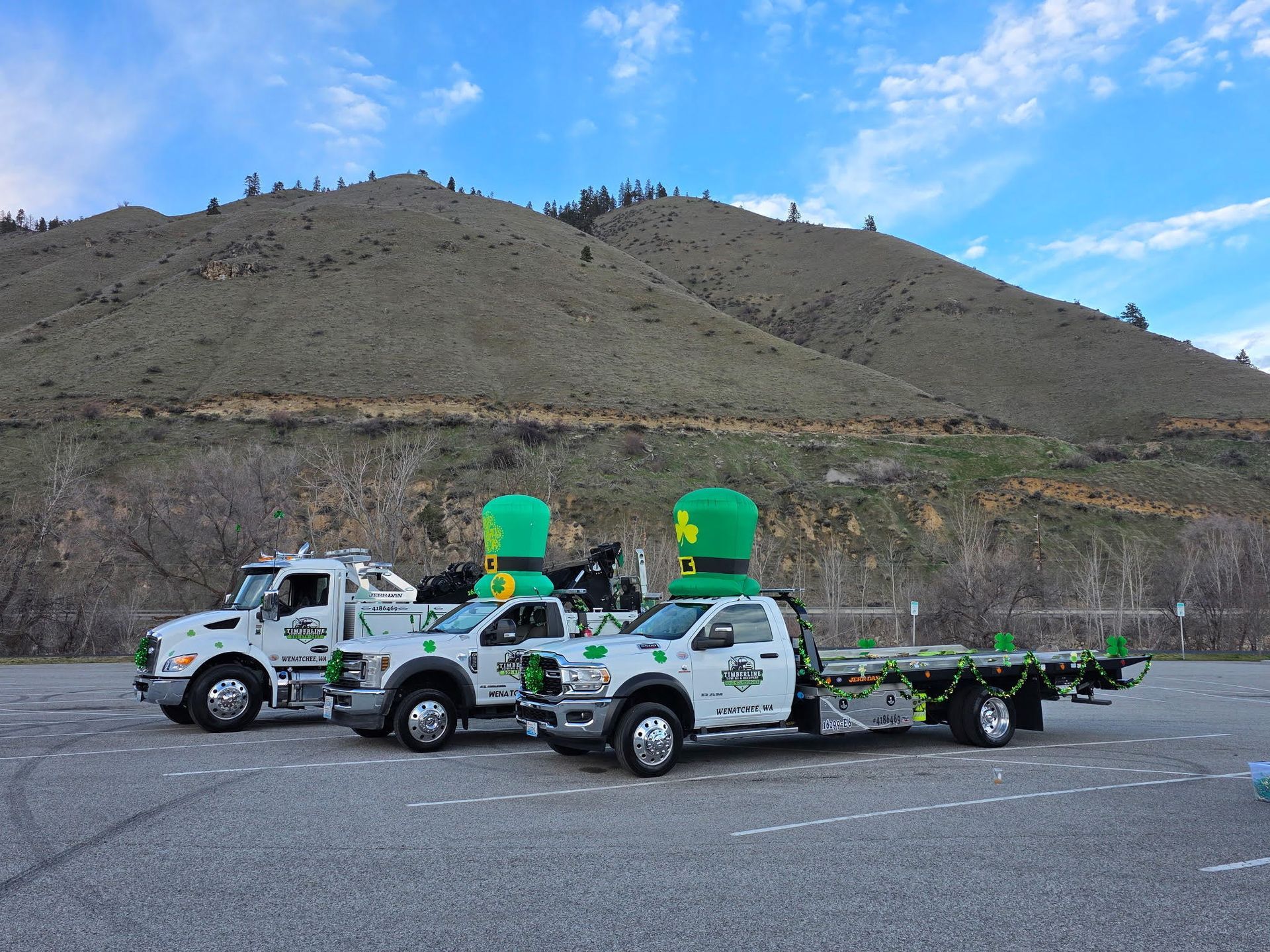 Three white trucks with bright green tanks parked on a lot, with hills in the background.