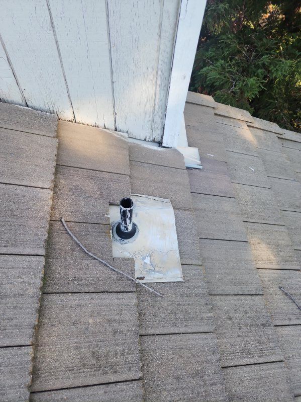 Close-up of a roof with a vent pipe; shingles are weathered, a white trim board sits above.