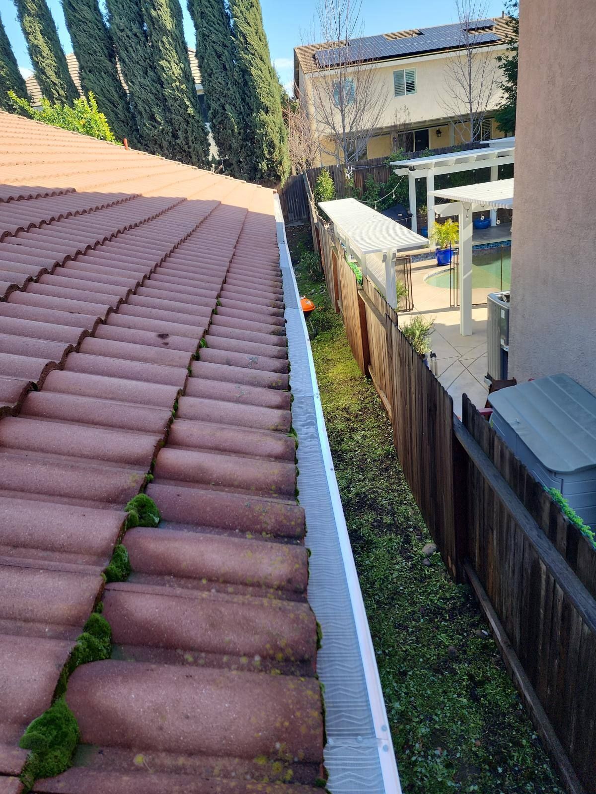 Red-tiled roof with gutter and fence separating the house from grassy area.