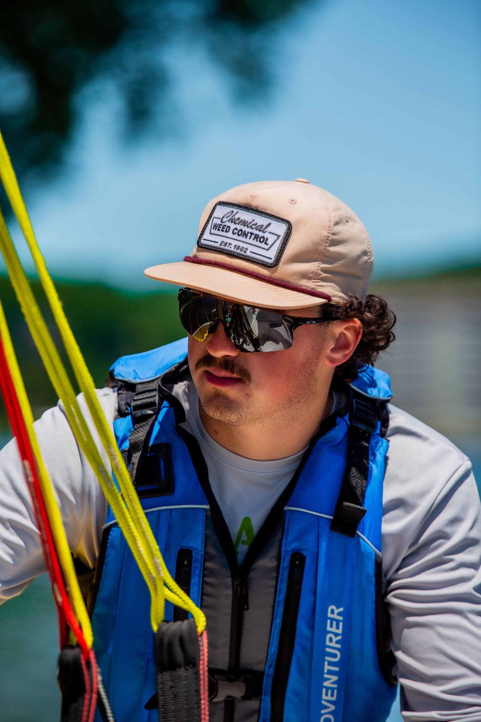 Man in a life vest and hat looking to the side, holding ropes.