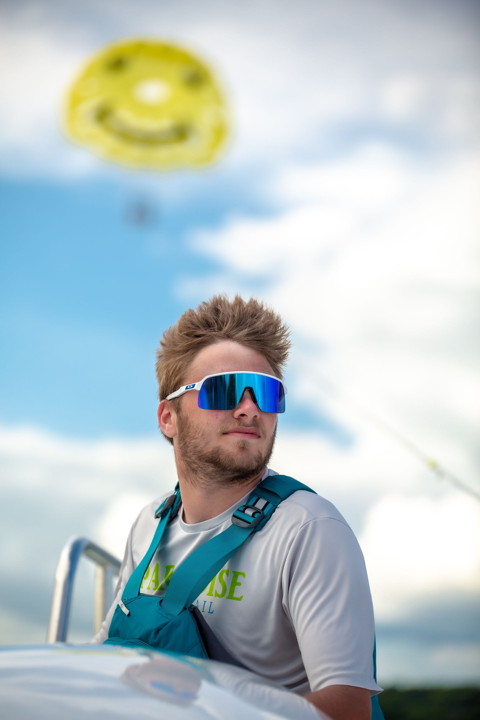 Man wearing sunglasses looks at parasail with smiley face in blue sky.