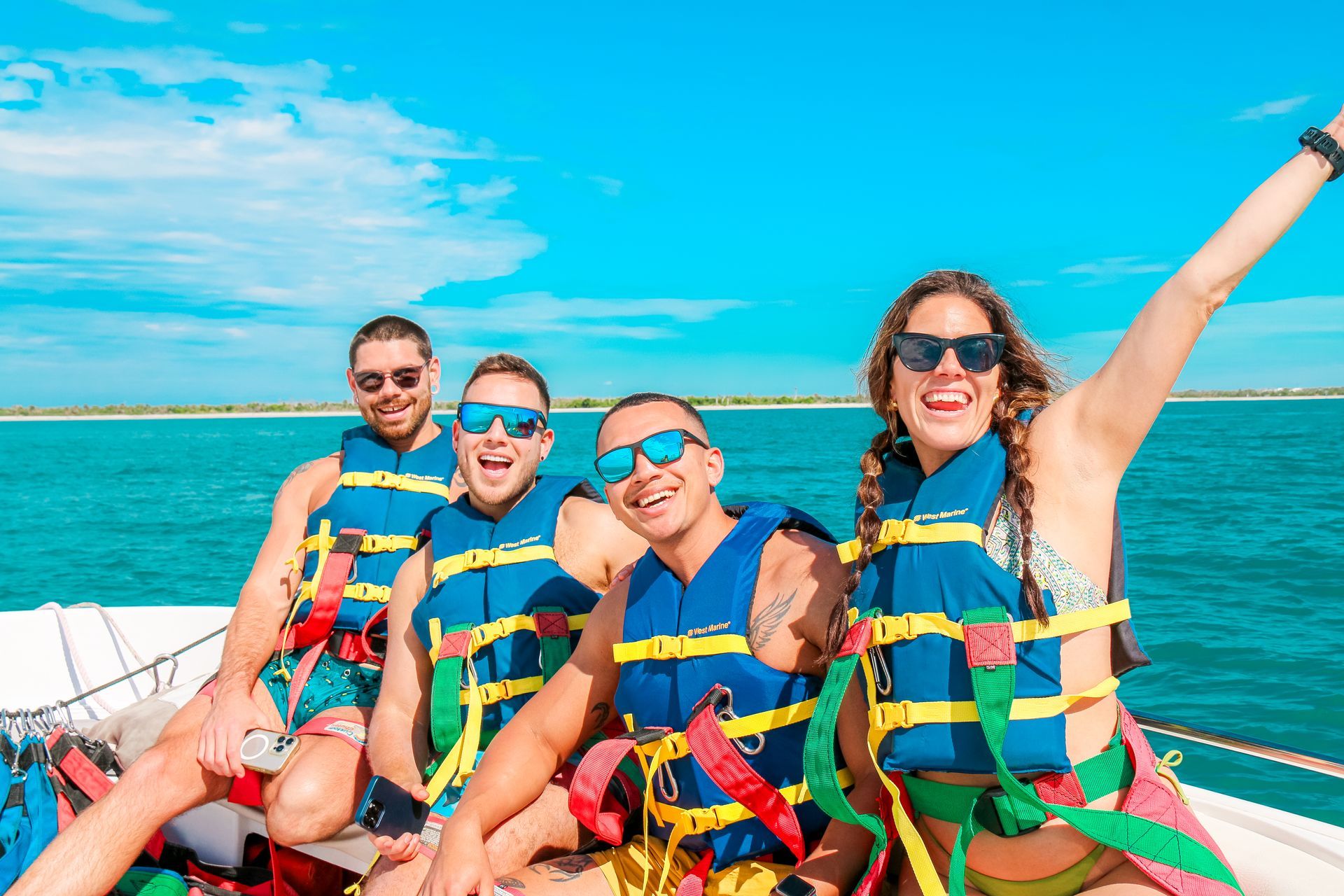 Four people on a boat wearing life vests, smiling under a bright blue sky.