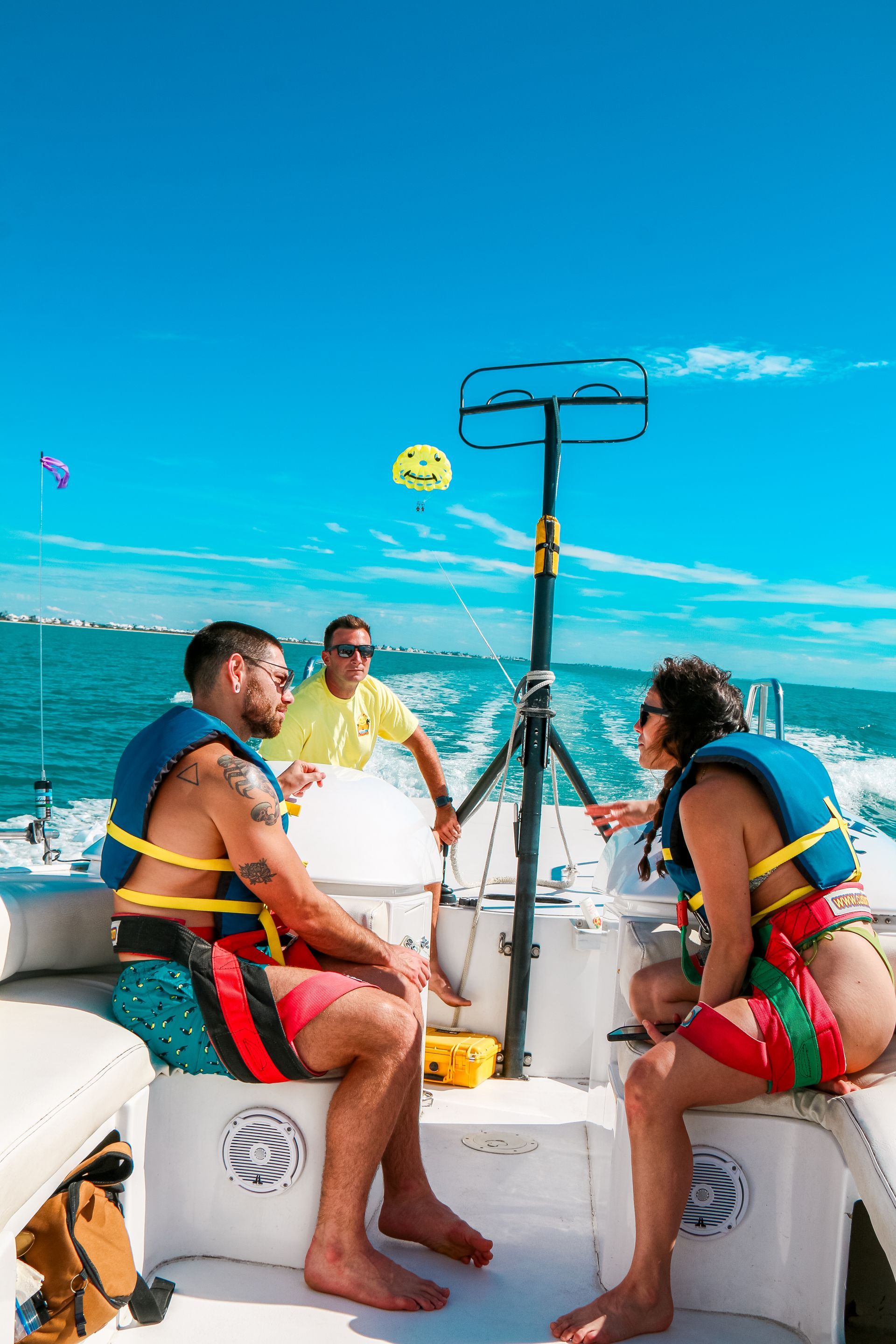 Two people on a boat about to parasail. Blue water, clear sky. Person in yellow shirt operates the equipment.