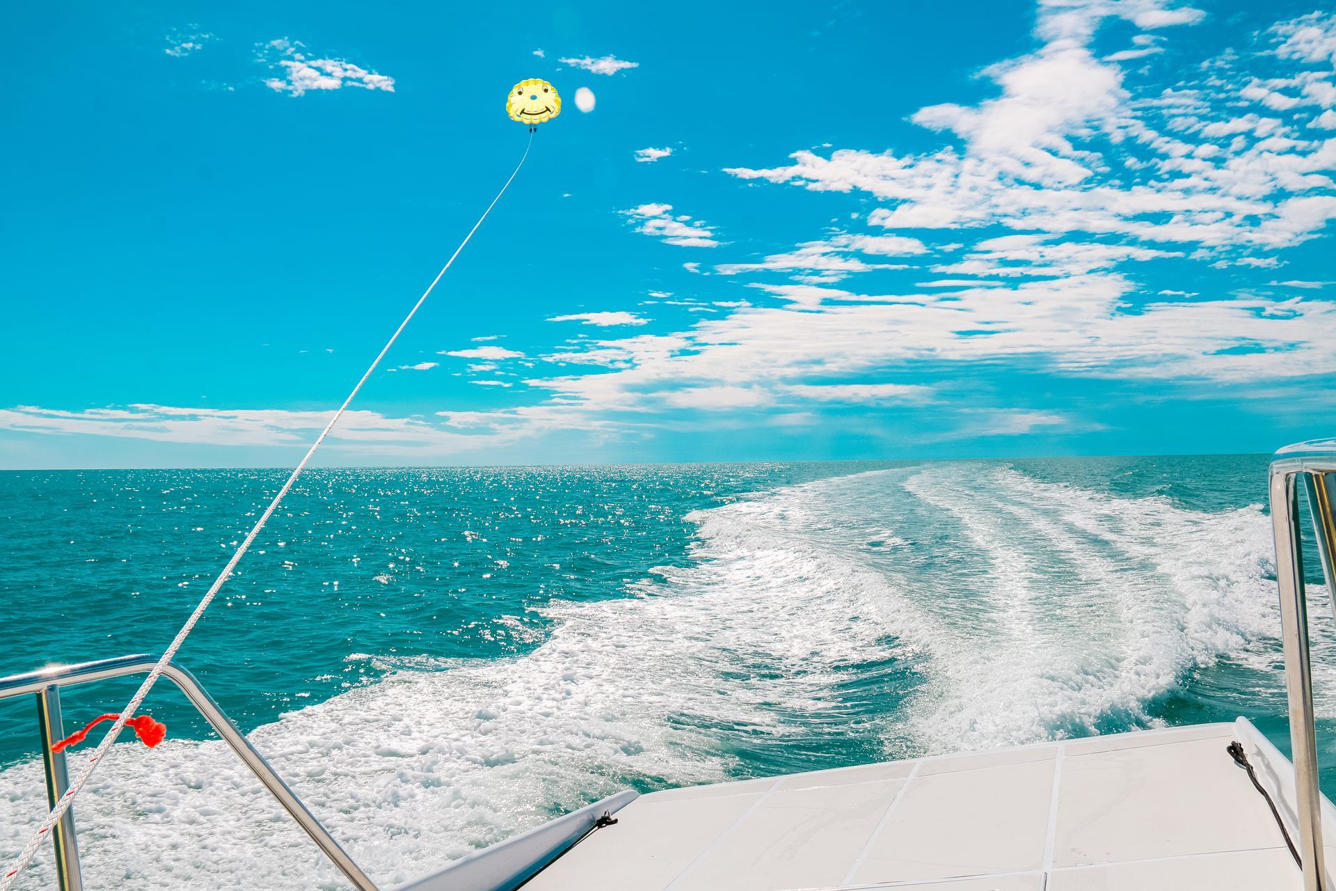 Boat towing parasail above ocean. Bright blue sky, sunny day.