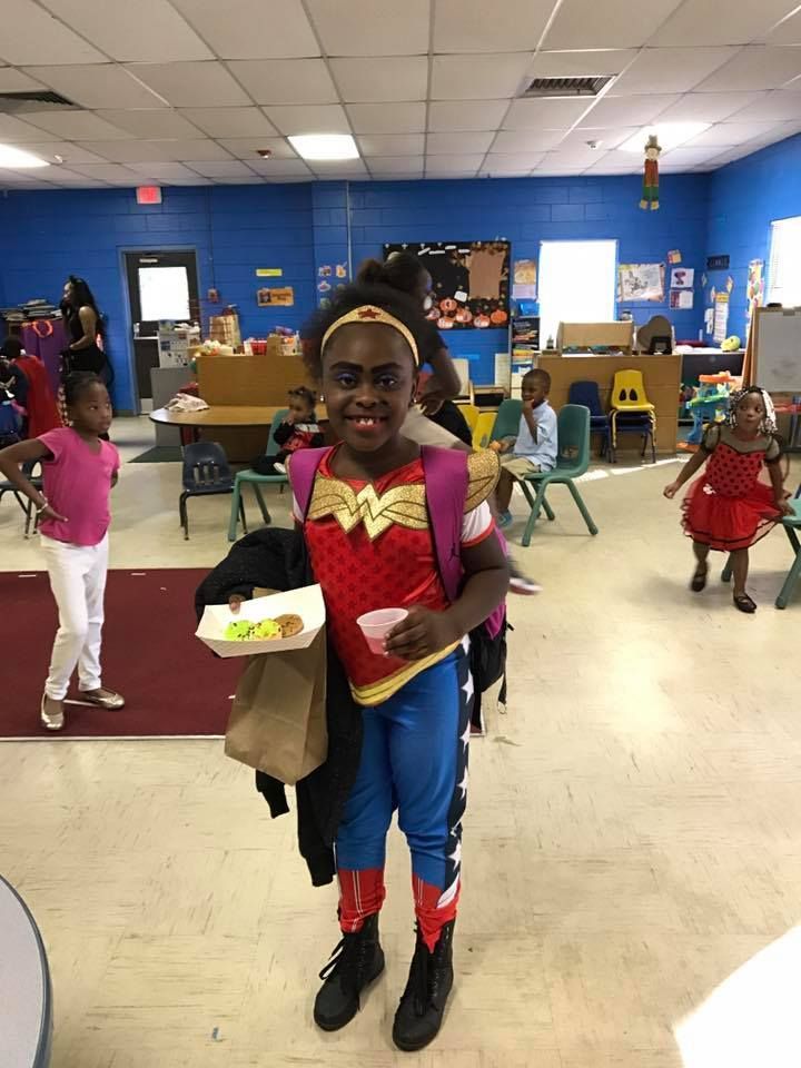 A young girl in a wonder woman costume is holding a tray of food.