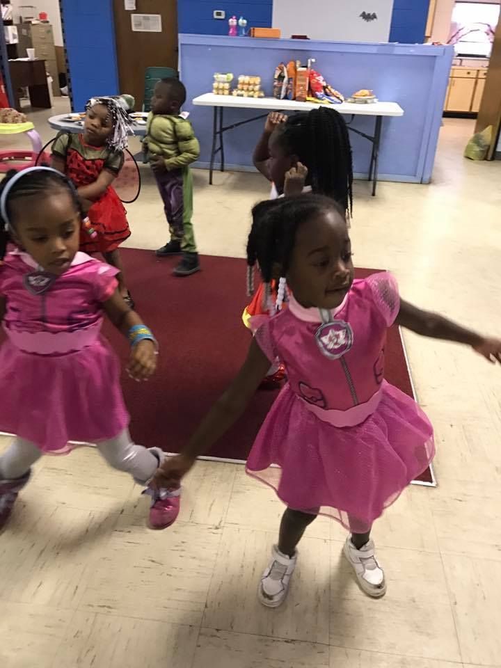 Two little girls in pink dresses are holding hands and dancing in a room.