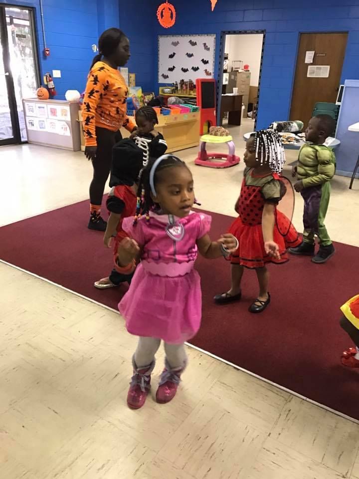A girl in a pink dress is dancing in a room with other children.