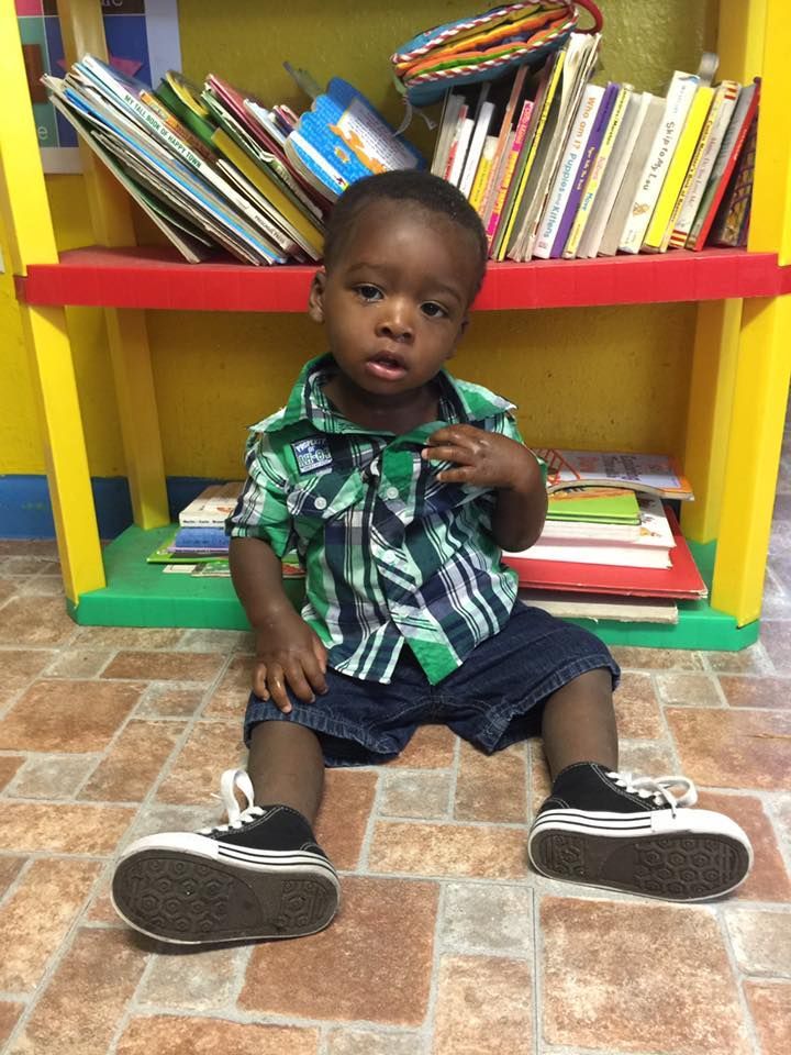 A young boy is sitting on the floor in front of a bookshelf.
