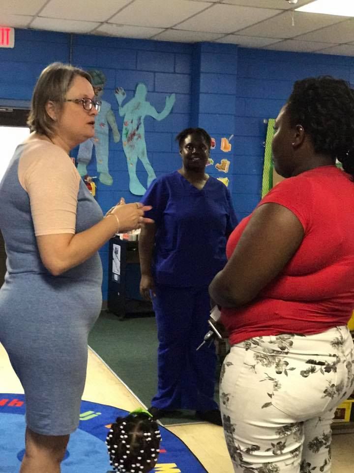 A woman in a blue dress is talking to another woman in a red shirt