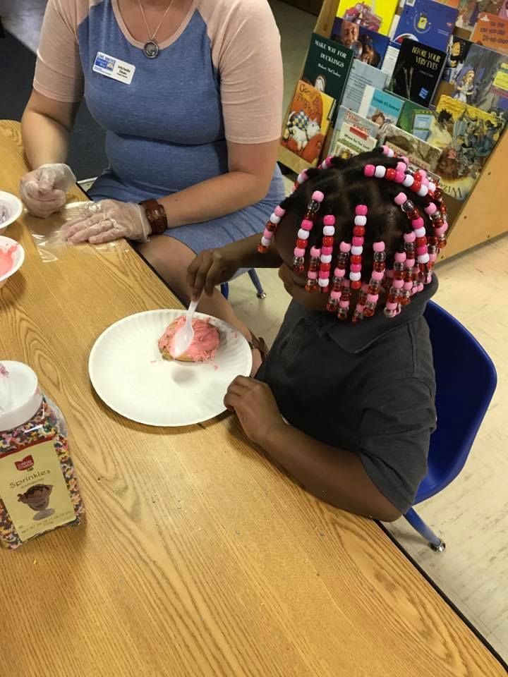 A woman and a child are sitting at a table decorating cookies.