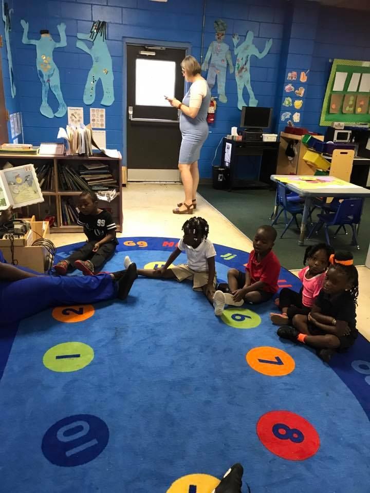 A group of children are sitting on a blue rug with numbers on it