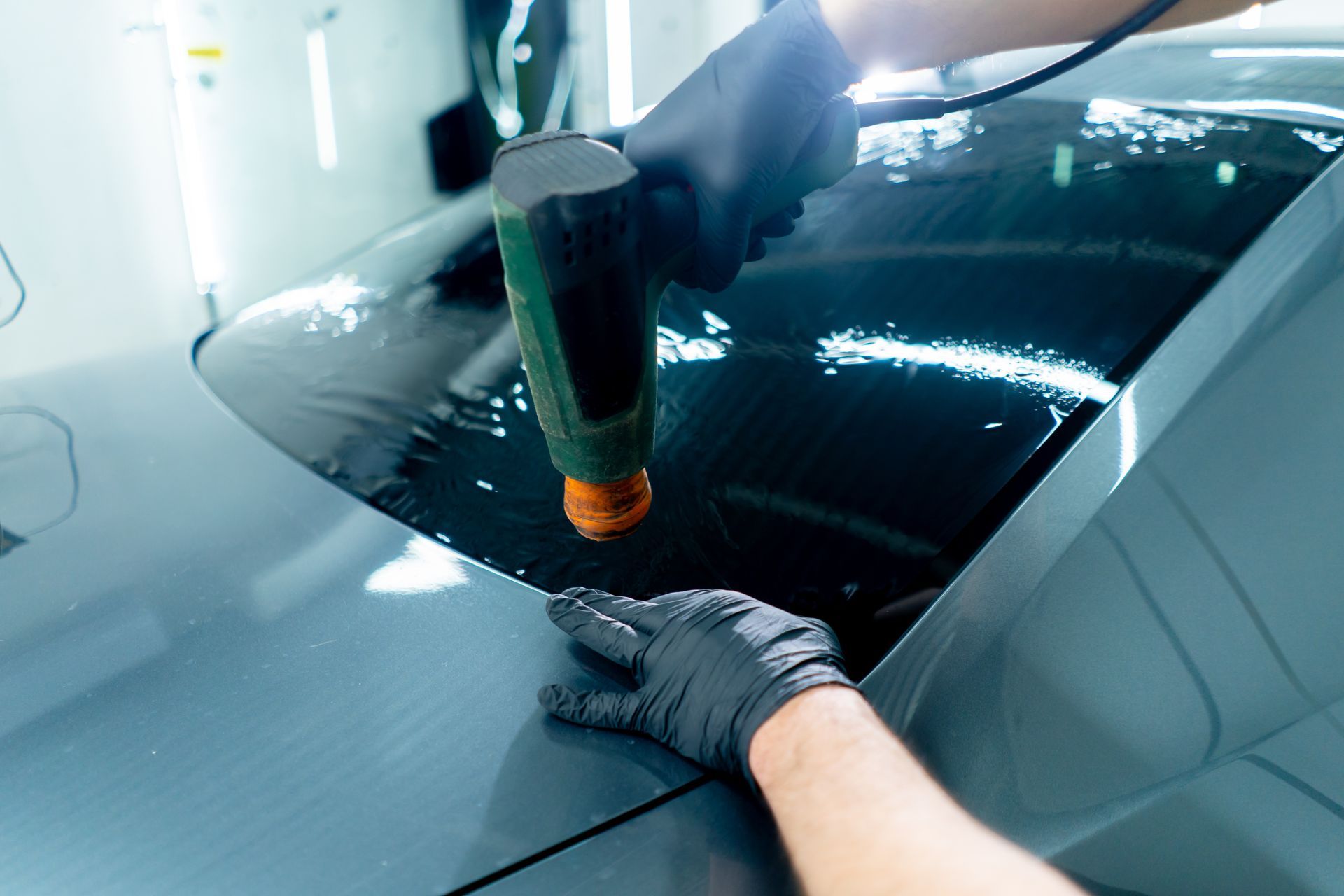 Gloved hand applying window film to a car windshield with a heat gun