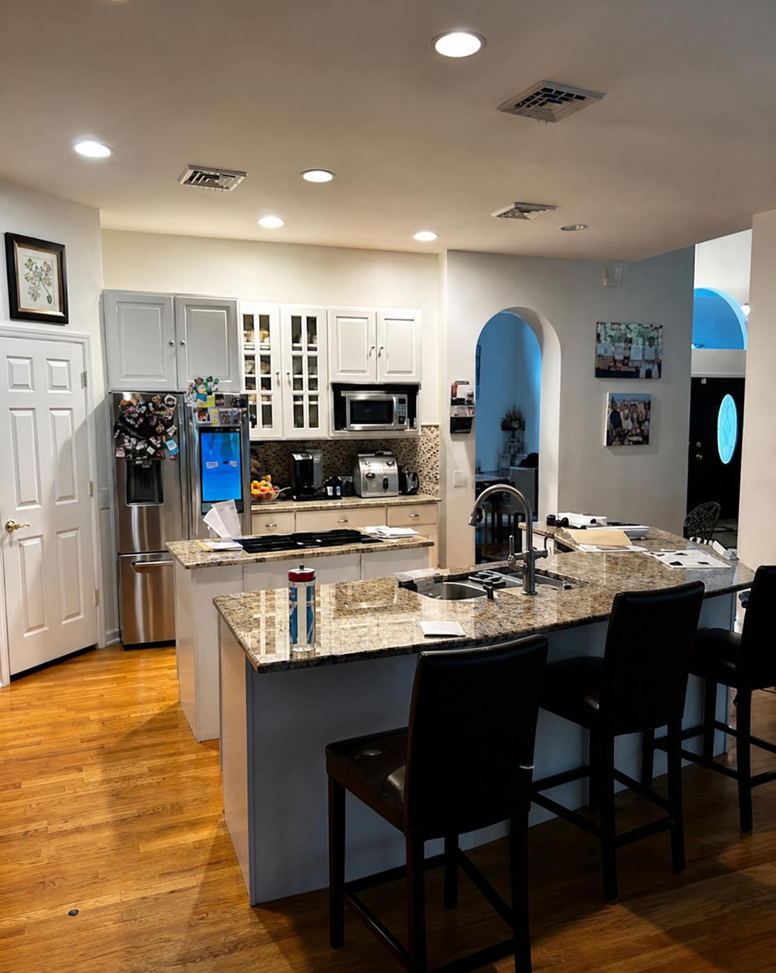Bright modern kitchen with granite island, stainless appliances, bar stools, and hardwood floors