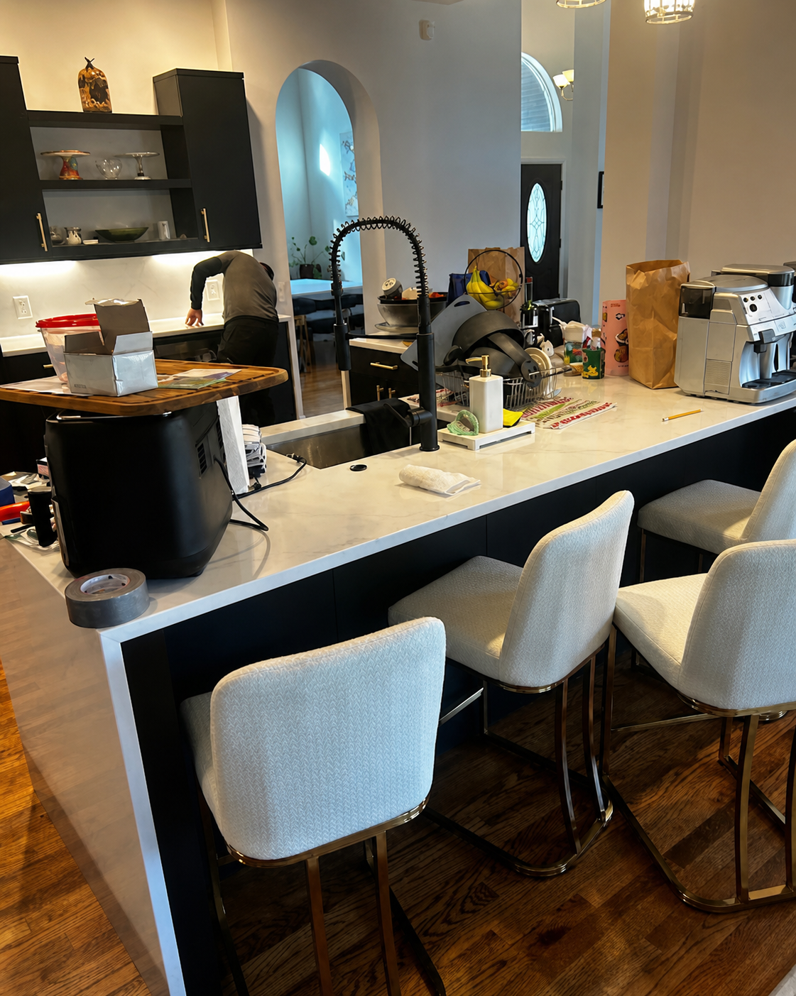 Modern kitchen island with white stools, countertop appliances, and bowls in a bright home interior