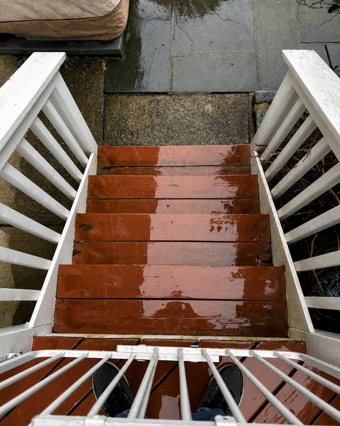 Rain-soaked wooden steps with white railings leading down to a wet landing