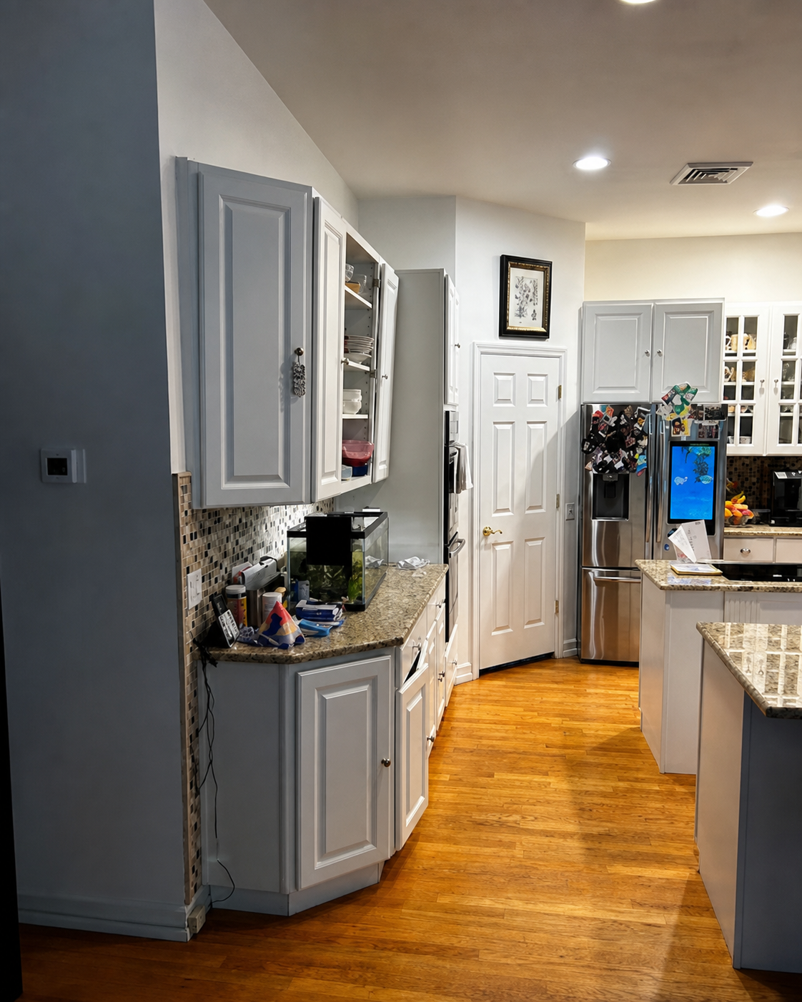 Bright kitchen with gray cabinets, granite countertops, stainless fridge, and warm hardwood floor in a home.