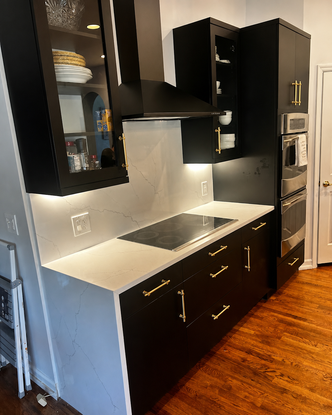 Modern kitchen with black cabinets, white countertop, built-in oven, and stainless-steel cooktop.