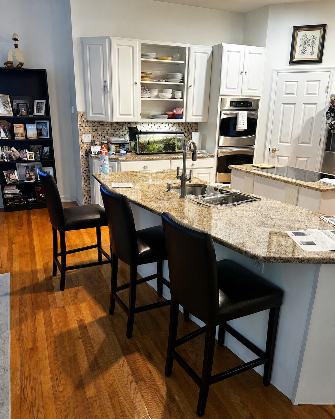 Modern kitchen with granite island, black bar stools, white cabinets, and hardwood floors.