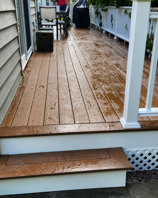 Weathered wooden porch and steps with white railing and wet surface after rain